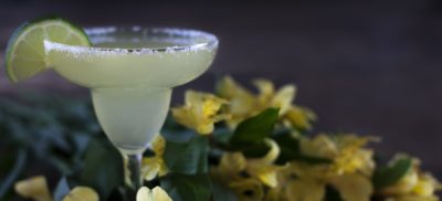 כוס מרגריטה עם פלח לימון וברקע פרחים צהובים מטושטשים