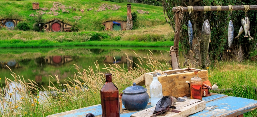 שולחן ארוחת בוקר מעץ על הדשא וברקע העיירה הוביטון